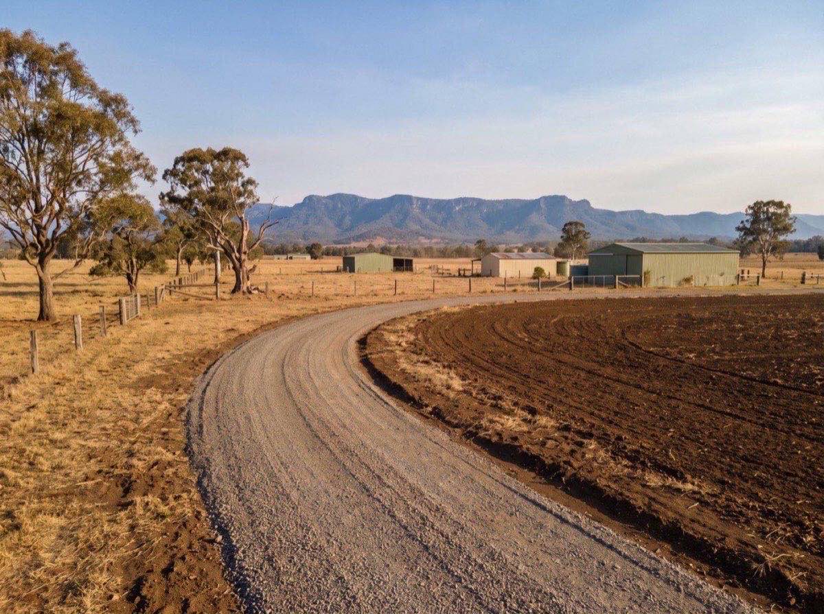 A freshly graded gravel driveway curving across rural acreage