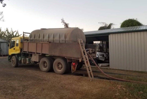 The water truck parked at a shed with the delivery hose running out