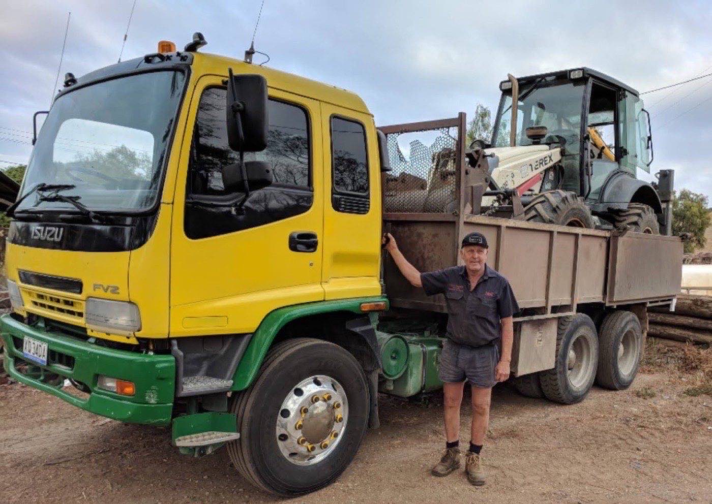 Neil standing beside the tip truck with the backhoe loaded on the tray