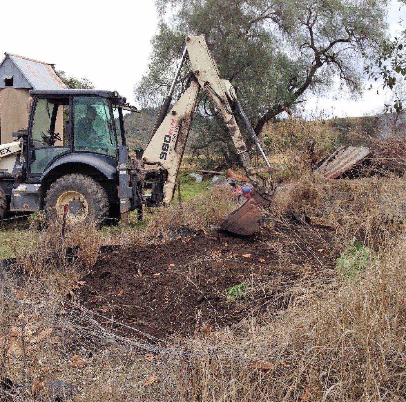 A backhoe digging out overgrown ground on a rural block
