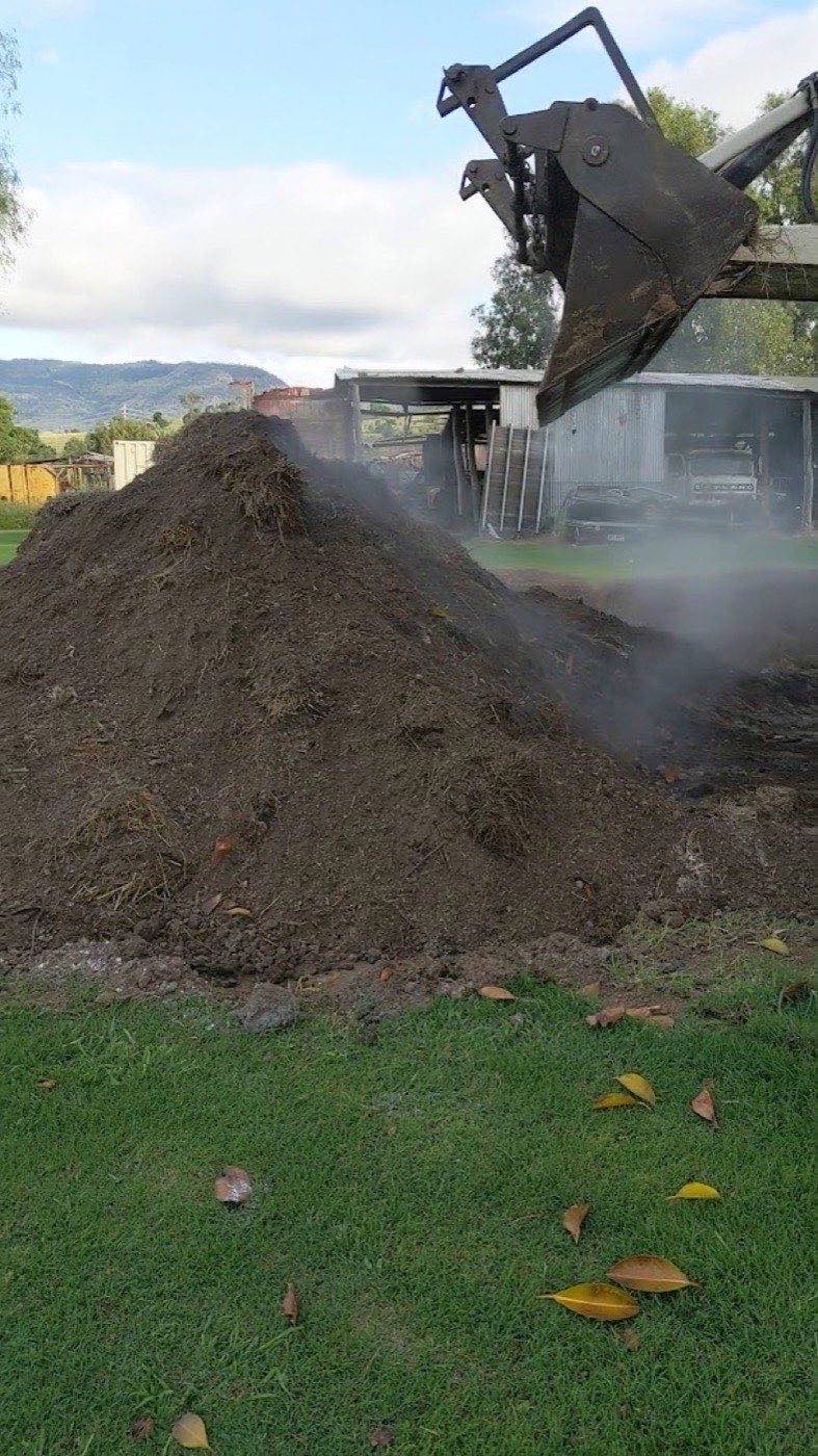 A steaming heap of screened topsoil being loaded on a rural property