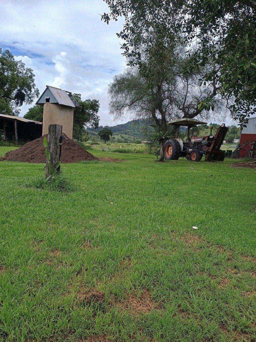 A delivered heap of topsoil beside a farm shed with the range behind